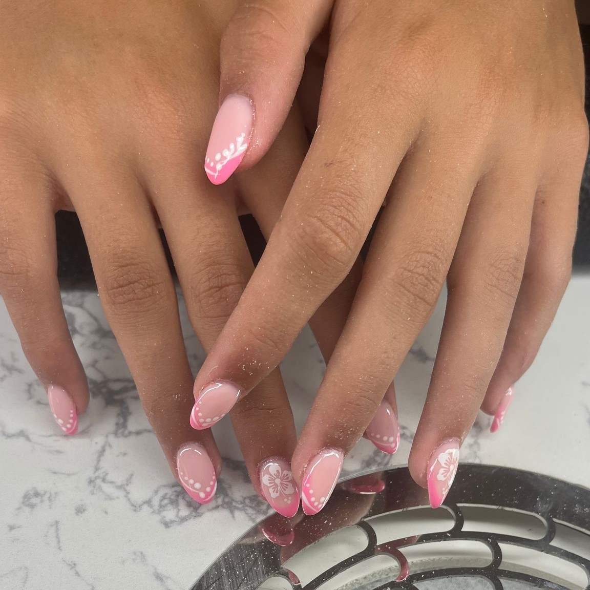 Twee handen met roze glitternagels in amandelvorm boven een zilveren schaal